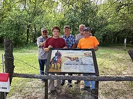 A plaque in front of a group of people, whom are themselves in front of a wooded area